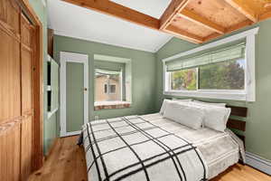 Apartment bedroom featuring light wood-style flooring, baseboard heating, and lofted ceiling with beams, closet, builtin shelves, north and west facing windows