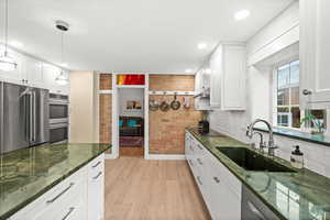 Kitchen with white cabinetry, stainless steel appliances, green granite counters, exposed brick wall, and tile floor