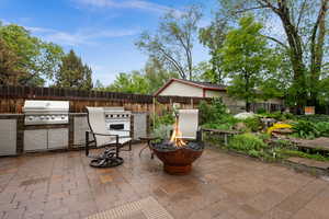 Fenced backyard featuring outdoor kitchen with pizza oven, grill and cooktop, a plumbed gas fire pit