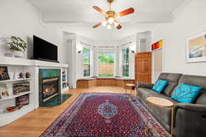 Living room with light wood-type flooring, a ceiling fan, a high end fireplace, and beamed ceiling