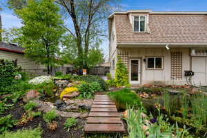 Back of house featuring a water fountain wooden path, a garden koi pond and beautifully landscaped perennial garden beds
