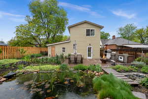Back of property with a fenced backyard, an outdoor kitchen / dining area, a koi pond and vegetable garden