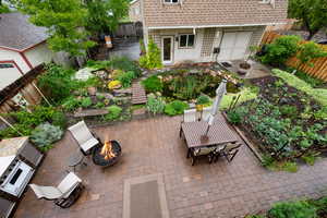 Back of house with an gas plumbed outdoor fire pit, a fenced backyard, a water feature, koi pond, and a patio area outdoor kithchen including a wood fired pizza oven, gas grill and cooktop