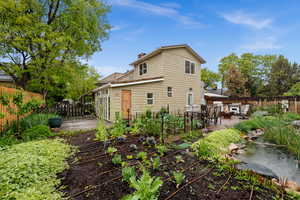 Back of house with a fenced backyard, a garden, flower beds and a patio and pond