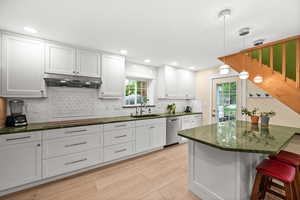 Kitchen featuring hanging light fixtures, white cabinetry, a breakfast bar area, and light wood-style flooring