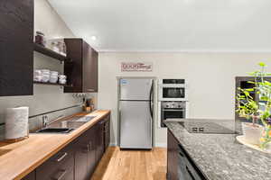 Kitchen featuring stainless steel appliances, dishwasher, wall oven and microwave, countertop cooktop, dark wood finish cabinetry, and open shelves