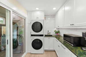 Main floor laundry area with stacked washer and dryer, sink, storage cabinets