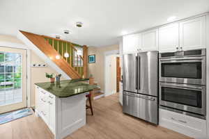 Kitchen with white cabinets, stainless steel appliances, a kitchen breakfast bar, and dark stone countertops