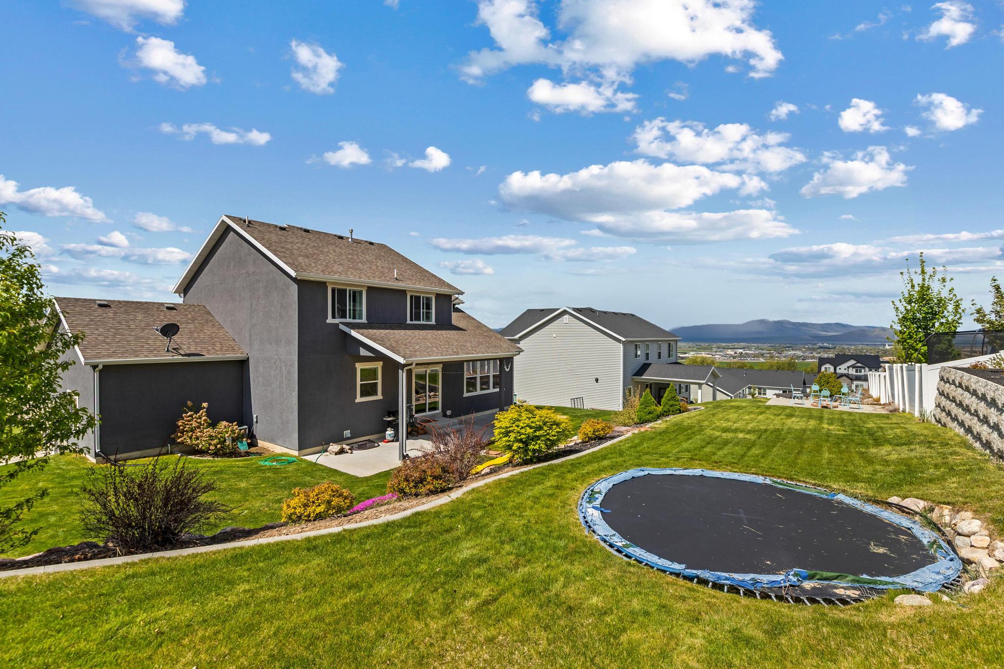 Back of house featuring a patio area, a trampoline, and a shingled roof