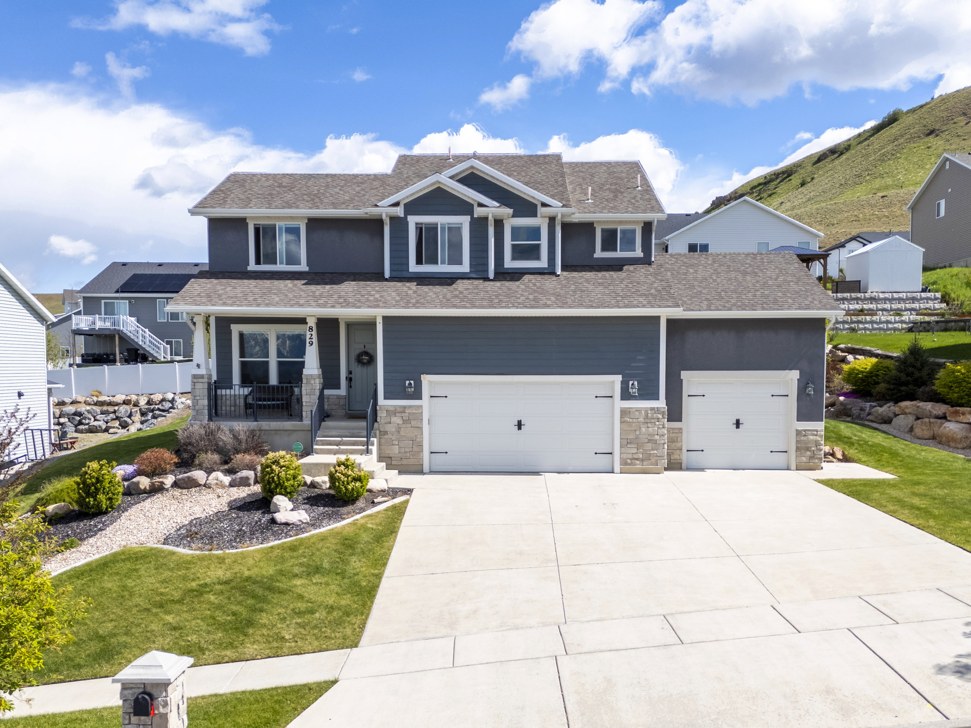 Craftsman-style house with covered porch, an attached garage, concrete driveway, stone siding, and a front lawn