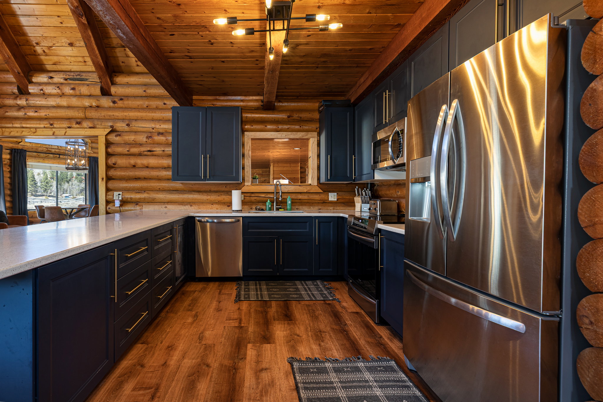 Kitchen with log walls, stainless steel appliances, dark wood-style floors, a peninsula, and a wooden ceiling with exposed beams