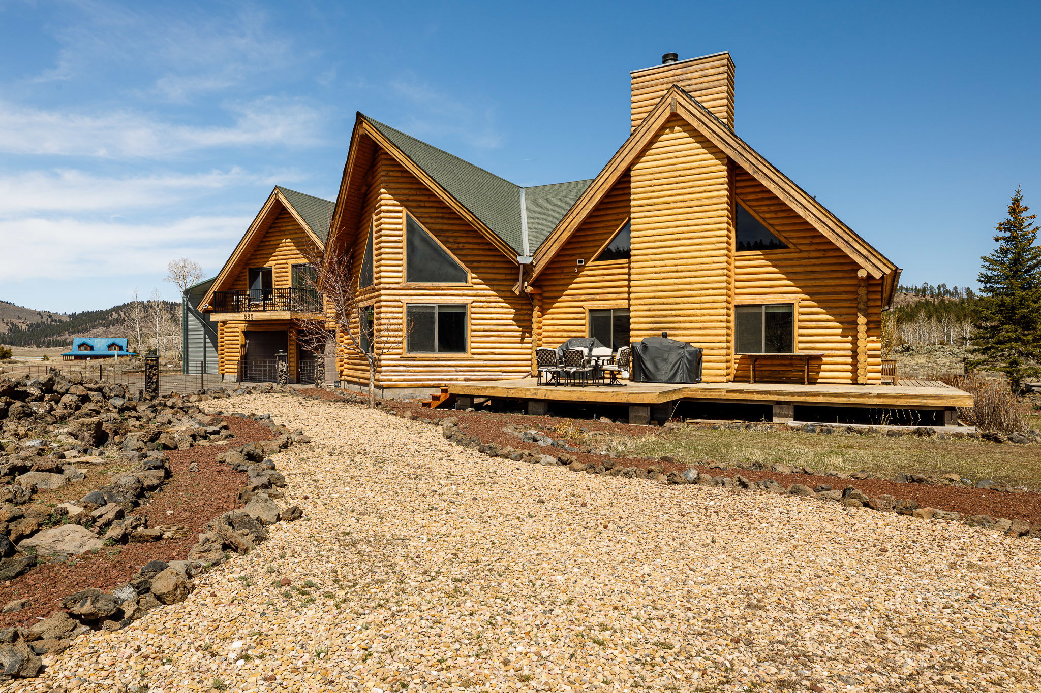 View of property exterior with log exterior, a wooden deck, a chimney, and a garage