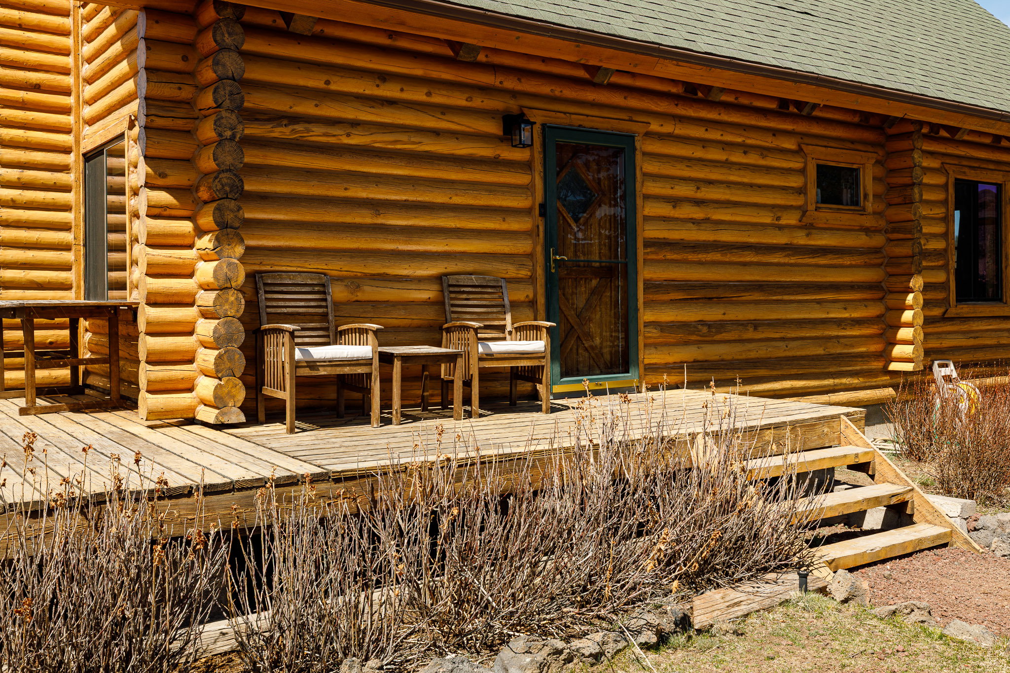 View of exterior entry featuring log exterior, a wooden deck, and a shingled roof
