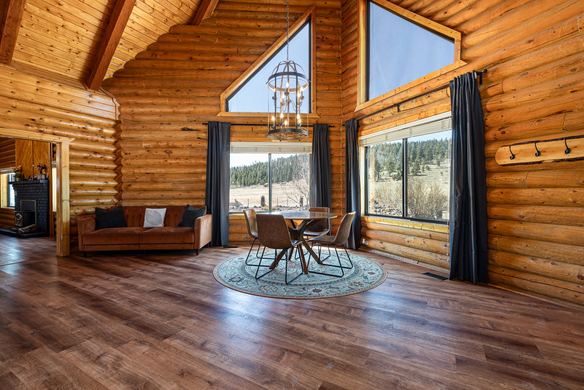 Dining space featuring a chandelier, wood finished floors, log walls, and a high wooden beamed ceiling