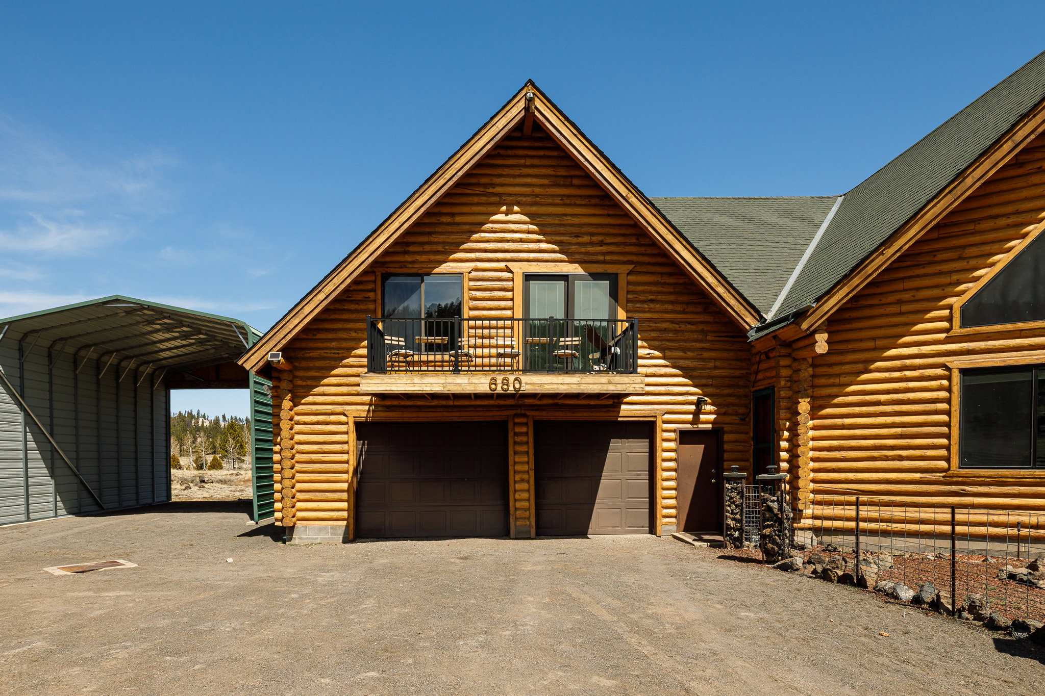 Log-style house featuring log exterior, a balcony, driveway, and a shingled roof