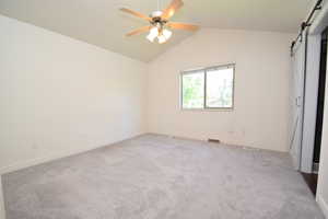 Unfurnished bedroom featuring a barn door, light carpet, and a ceiling fan
