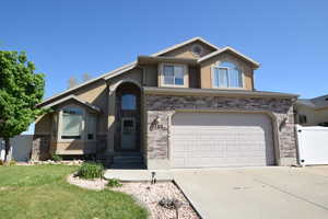 View of front of house with concrete driveway, stucco siding, a front yard, a garage, and brick siding