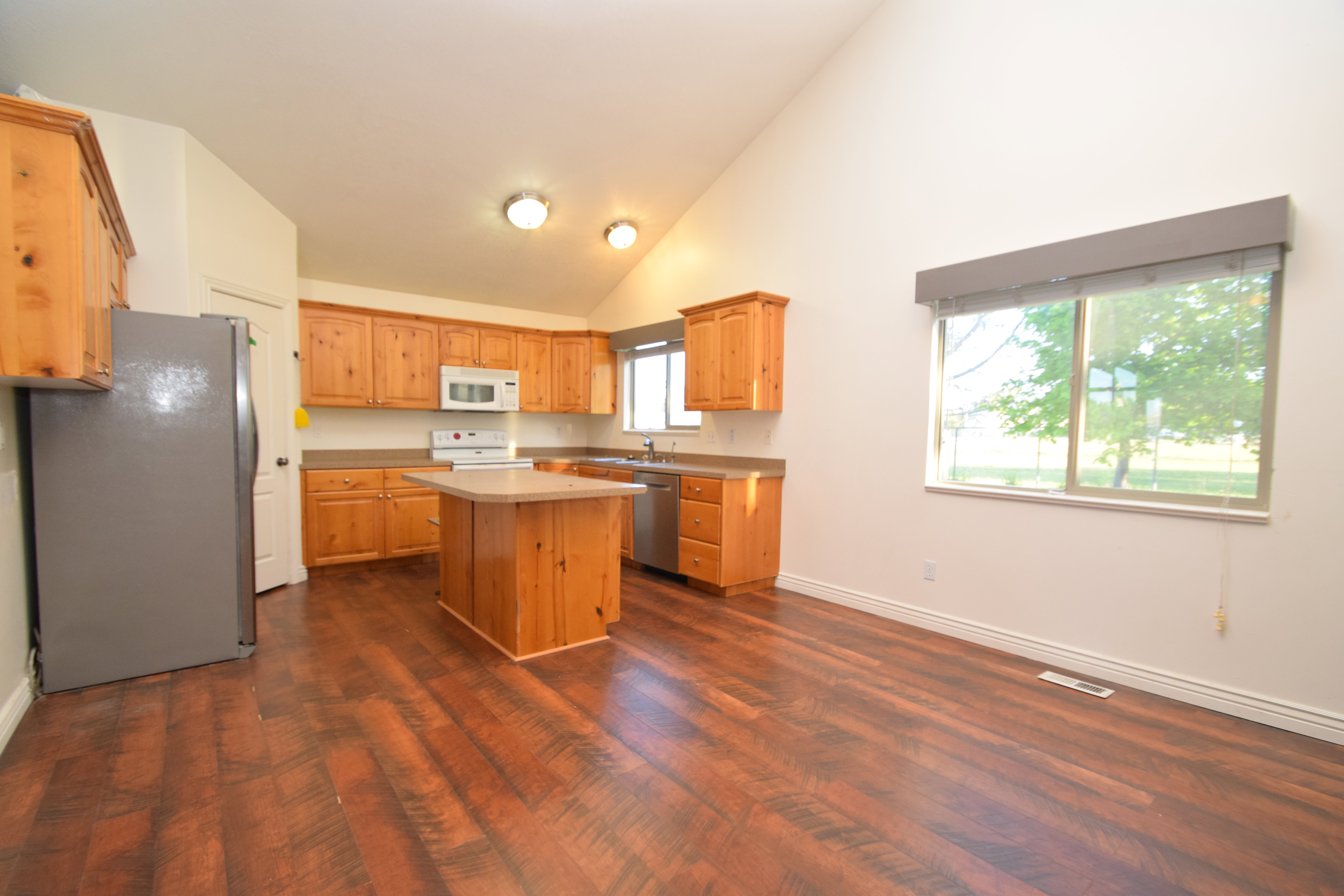 Kitchen with stainless steel appliances, a kitchen island, light countertops, vaulted ceiling, and dark wood-style flooring