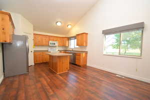 Kitchen with stainless steel appliances, a kitchen island, light countertops, vaulted ceiling, and dark wood-style flooring