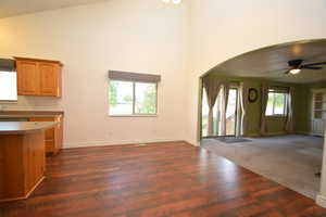 Kitchen with open floor plan, a ceiling fan, arched walkways, dark wood-style floors, and lofted ceiling