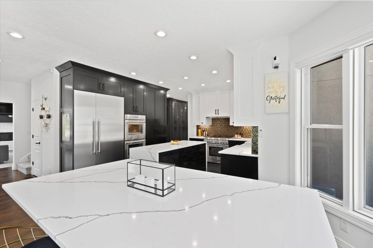 Two tone kitchen featuring a kitchen island, light stone counters, high quality appliances, tasteful backsplash, and two tone color scheme