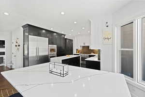 Two tone kitchen featuring a kitchen island, light stone counters, high quality appliances, tasteful backsplash, and two tone color scheme