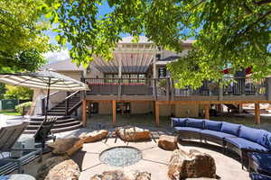 Rear view of property with a wooden deck, a patio, an outdoor living space with a fire pit, a shingled roof, and stucco siding