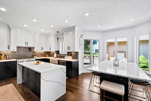 Kitchen featuring two tone cabinetry, a center island, light stone counters, dark wood-type flooring, and a kitchen bar