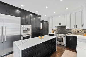 Kitchen featuring light stone countertops, high end appliances, recessed lighting, two tone cabinets, and tasteful backsplash