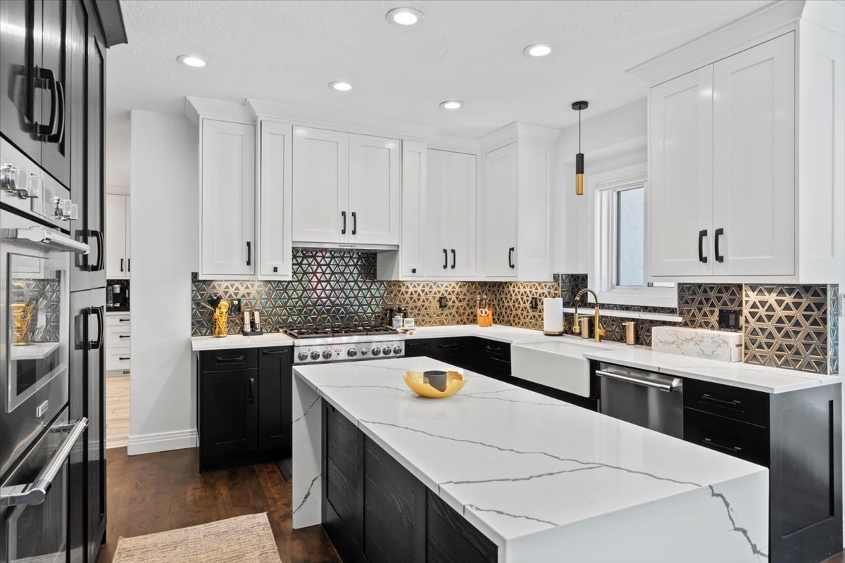 Two tone kitchen with dual tone cabinets, hanging light fixtures, light stone counters, dark wood-style floors, and stainless steel appliances
