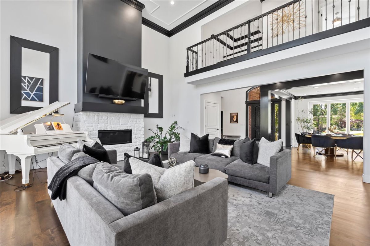 Living room with crown molding, a high ceiling, wood finished floors, and a stone fireplace