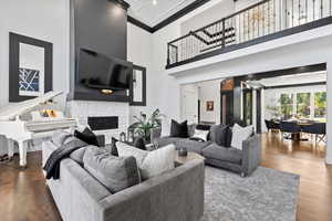 Living room with crown molding, a high ceiling, wood finished floors, and a stone fireplace