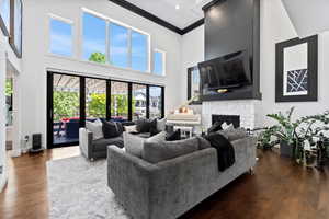 Living room featuring ornamental molding, a stone fireplace, a high ceiling, and dark wood-type flooring