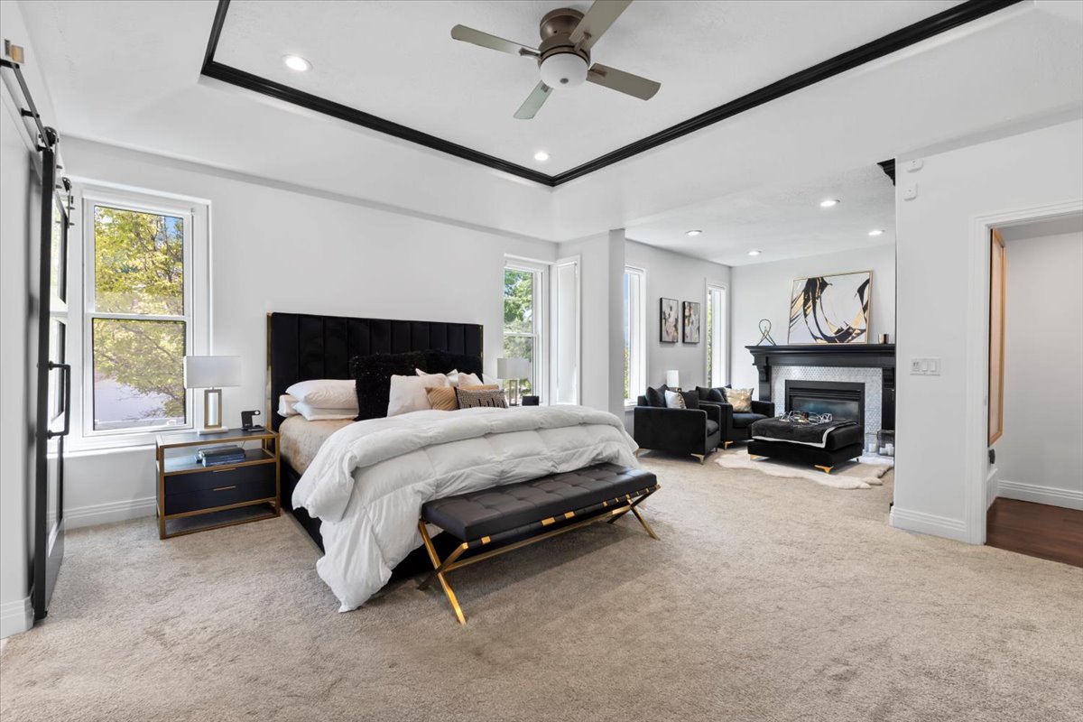 Carpeted bedroom featuring a glass covered fireplace, recessed lighting, multiple windows, a ceiling fan, and a barn door