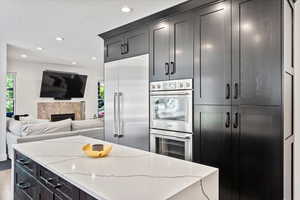 Kitchen featuring recessed lighting, open floor plan, stainless steel appliances, dark cabinetry, and light stone countertops