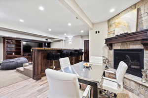 Dining room featuring light wood finished floors, a bar, a stone fireplace, and recessed lighting