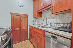 Kitchen featuring stainless steel appliances, light wood-style flooring, light stone countertops, backsplash, and wood finish cabinets