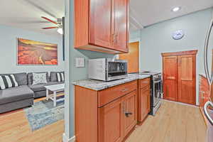 Kitchen with stainless steel appliances, light wood-style floors, light stone countertops, a ceiling fan, and wood finish cabinetry
