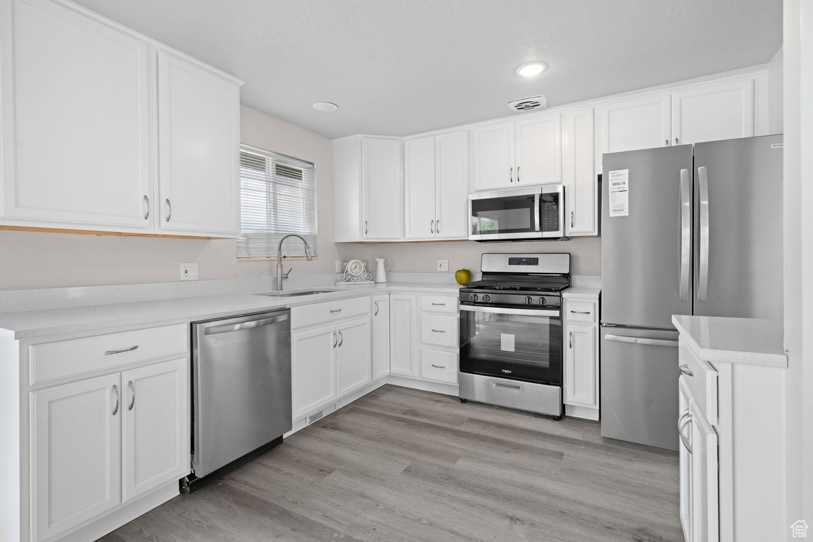 Kitchen with stainless steel appliances, white cabinets, light wood-style flooring, recessed lighting, and light stone countertops