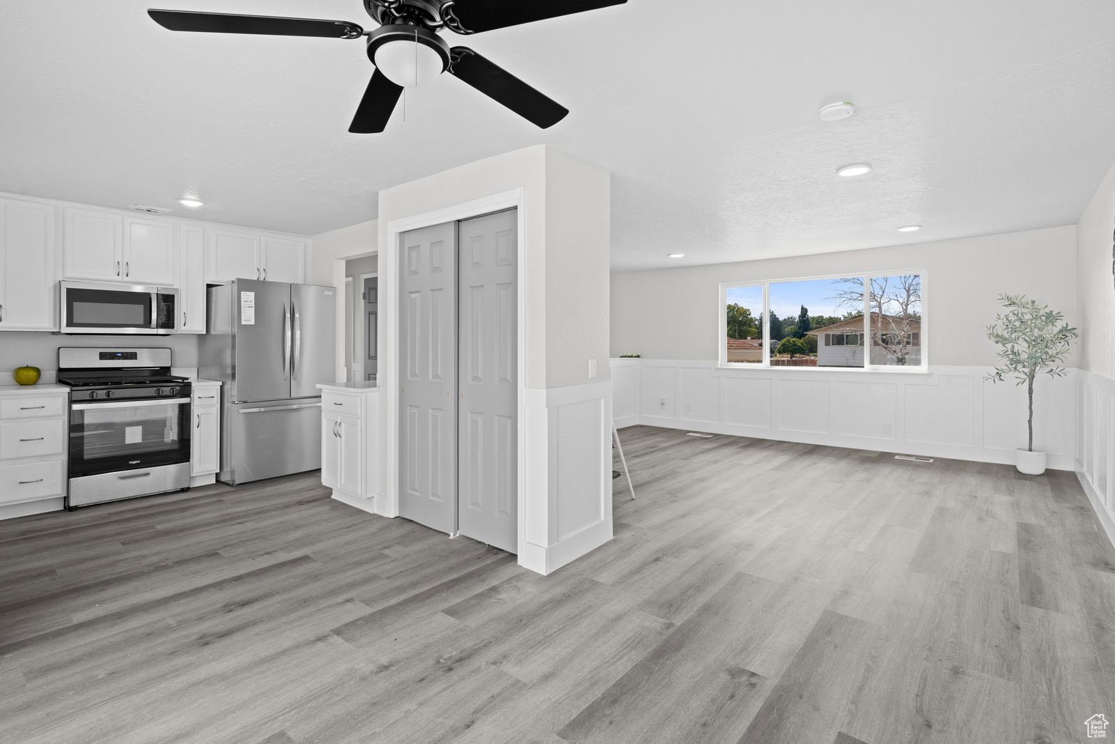 Kitchen featuring a wainscoted wall, light countertops, white cabinets, stainless steel appliances, and a ceiling fan