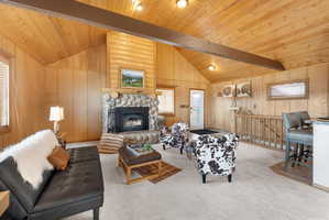 Carpeted living area featuring a fireplace, wooden walls, and vaulted ceiling