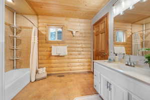 Full bathroom featuring wood ceiling, log walls, vanity, and shower / bath combo with shower curtain