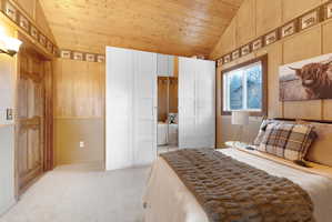 Bedroom featuring wood walls, light colored carpet, a wainscoted wall, a vaulted wood ceiling, and a decorative wall
