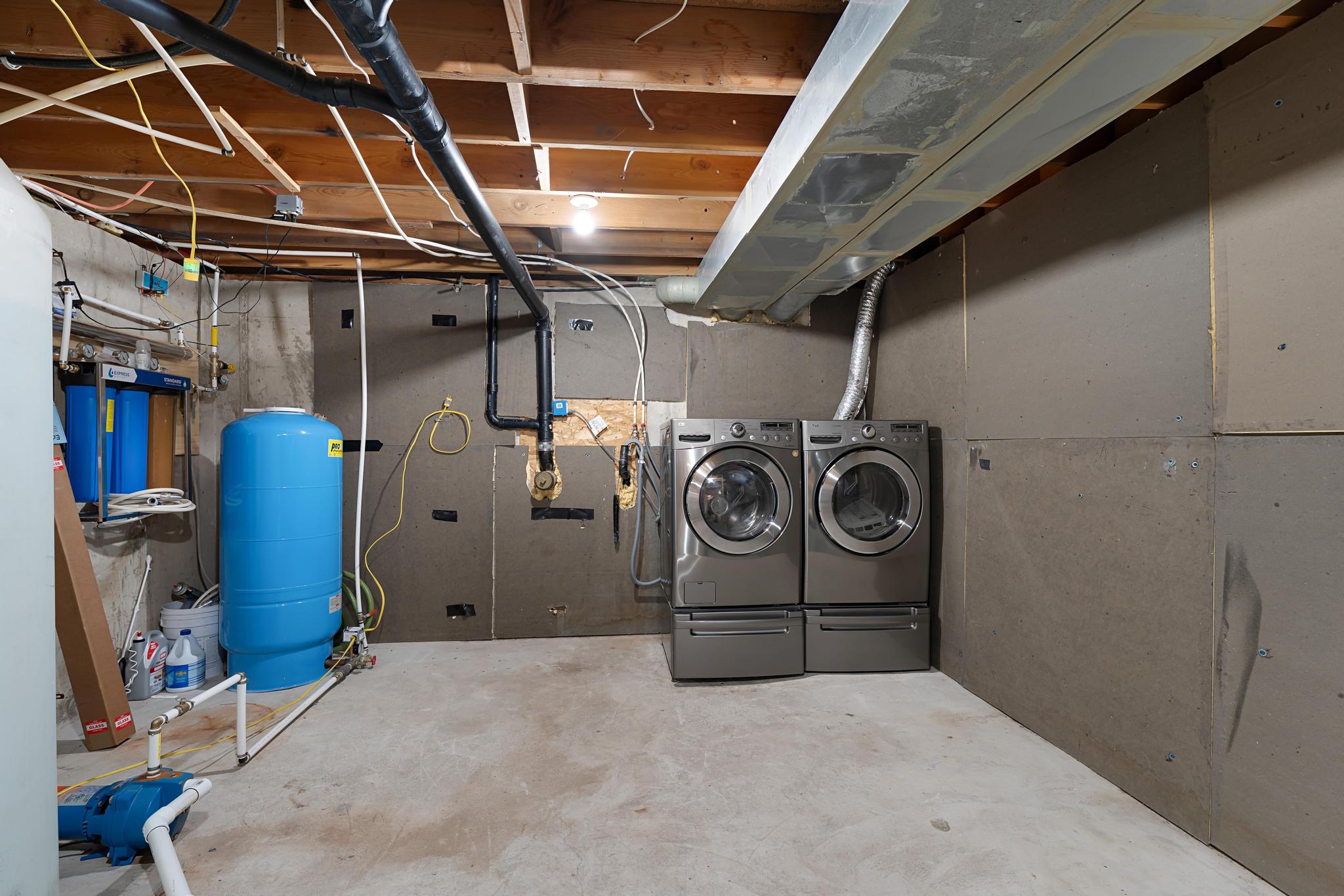 Unfinished below grade area featuring a water pressure tank and washing machine and clothes dryer