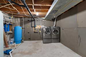 Unfinished below grade area featuring a water pressure tank and washing machine and clothes dryer