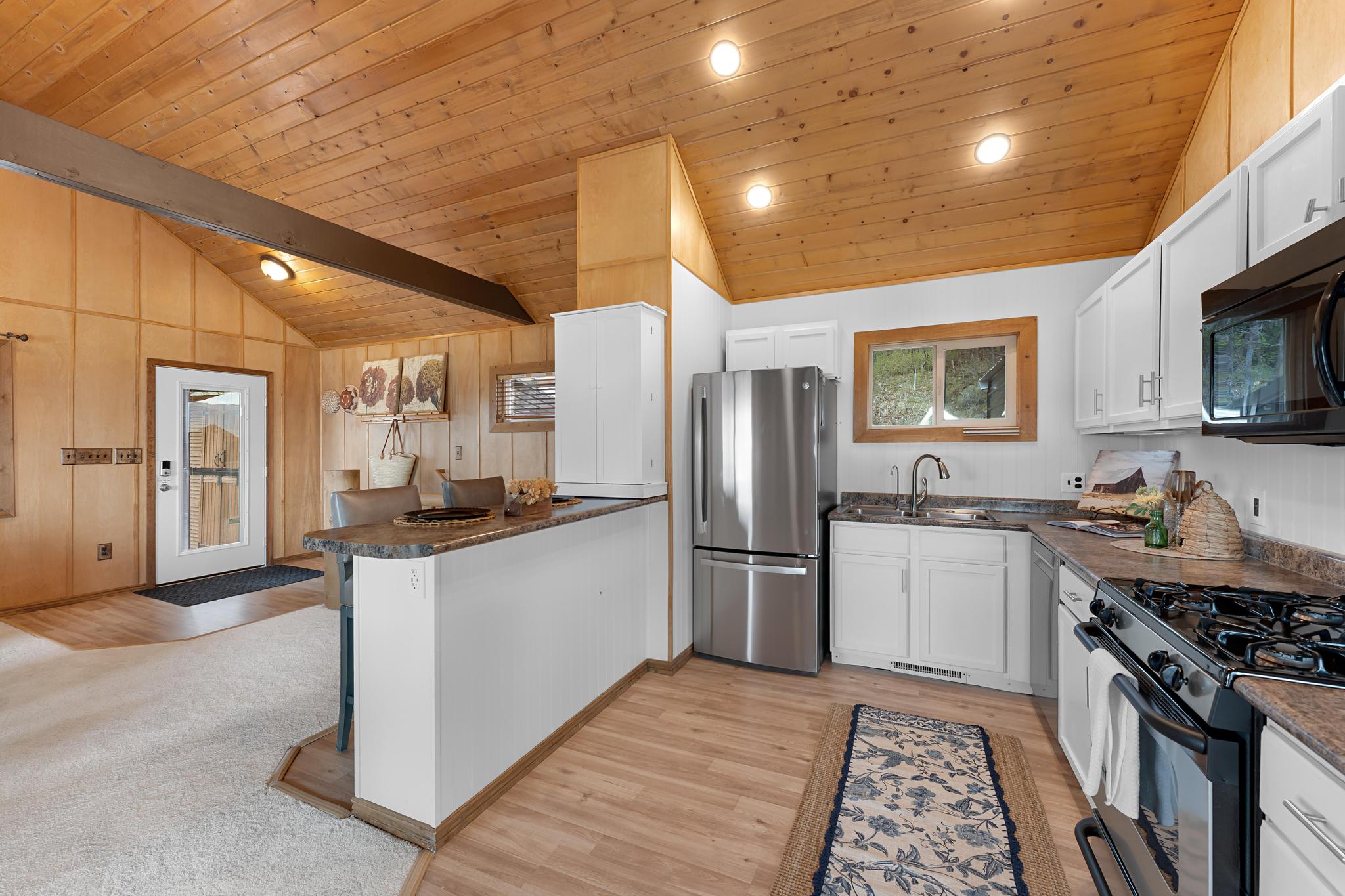 Kitchen featuring dark countertops, a peninsula, black appliances, a vaulted wooden ceiling, and white cabinets