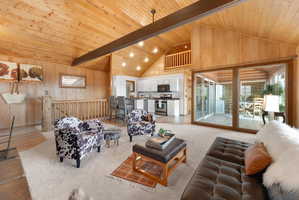 Living room featuring wooden walls, a high wood beamed ceiling, and light colored carpet