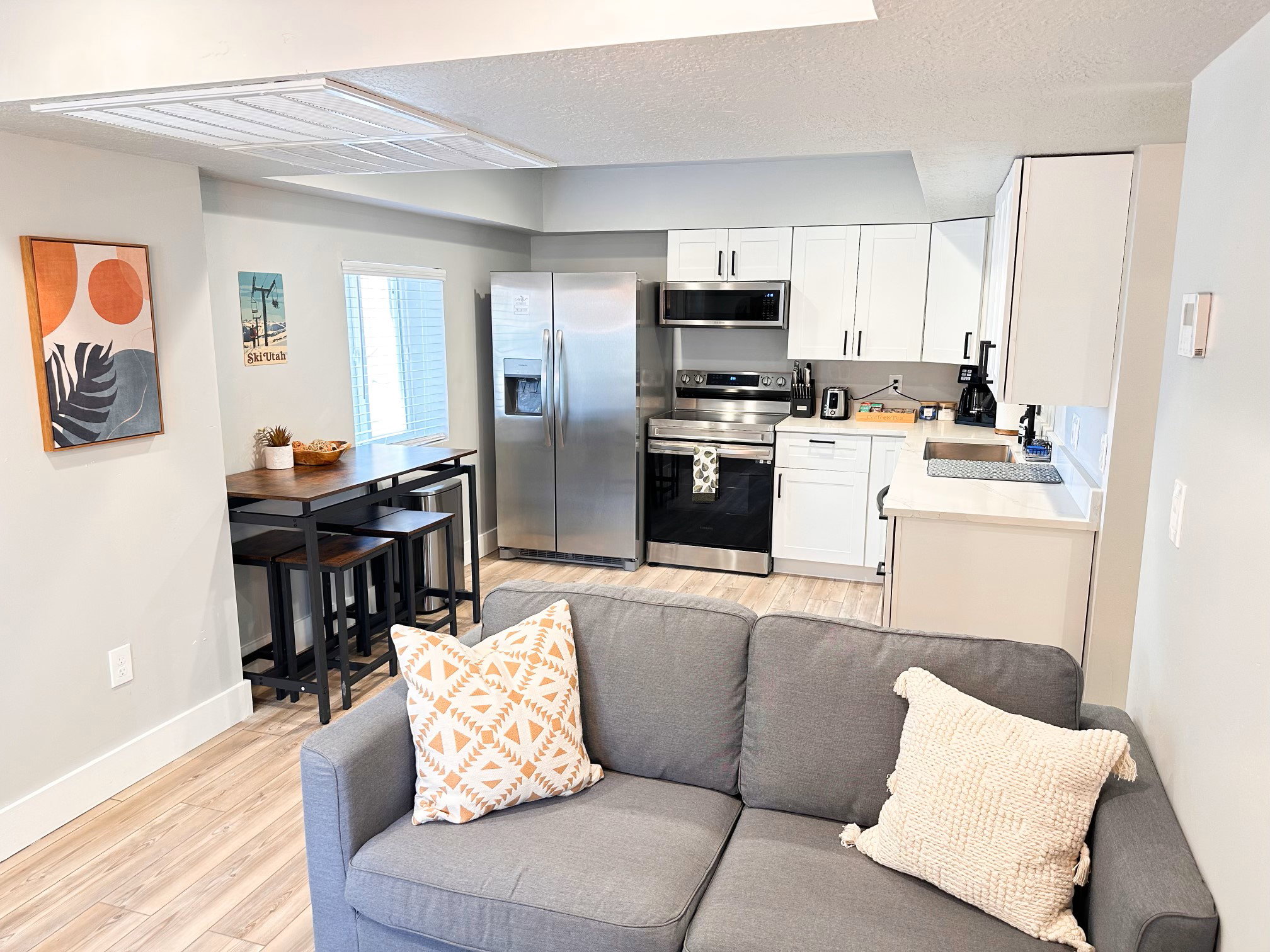 Furnished Unit #44 Kitchen featuring light wood-style floors, stainless steel appliances, white cabinets, a textured ceiling, and light stone counters