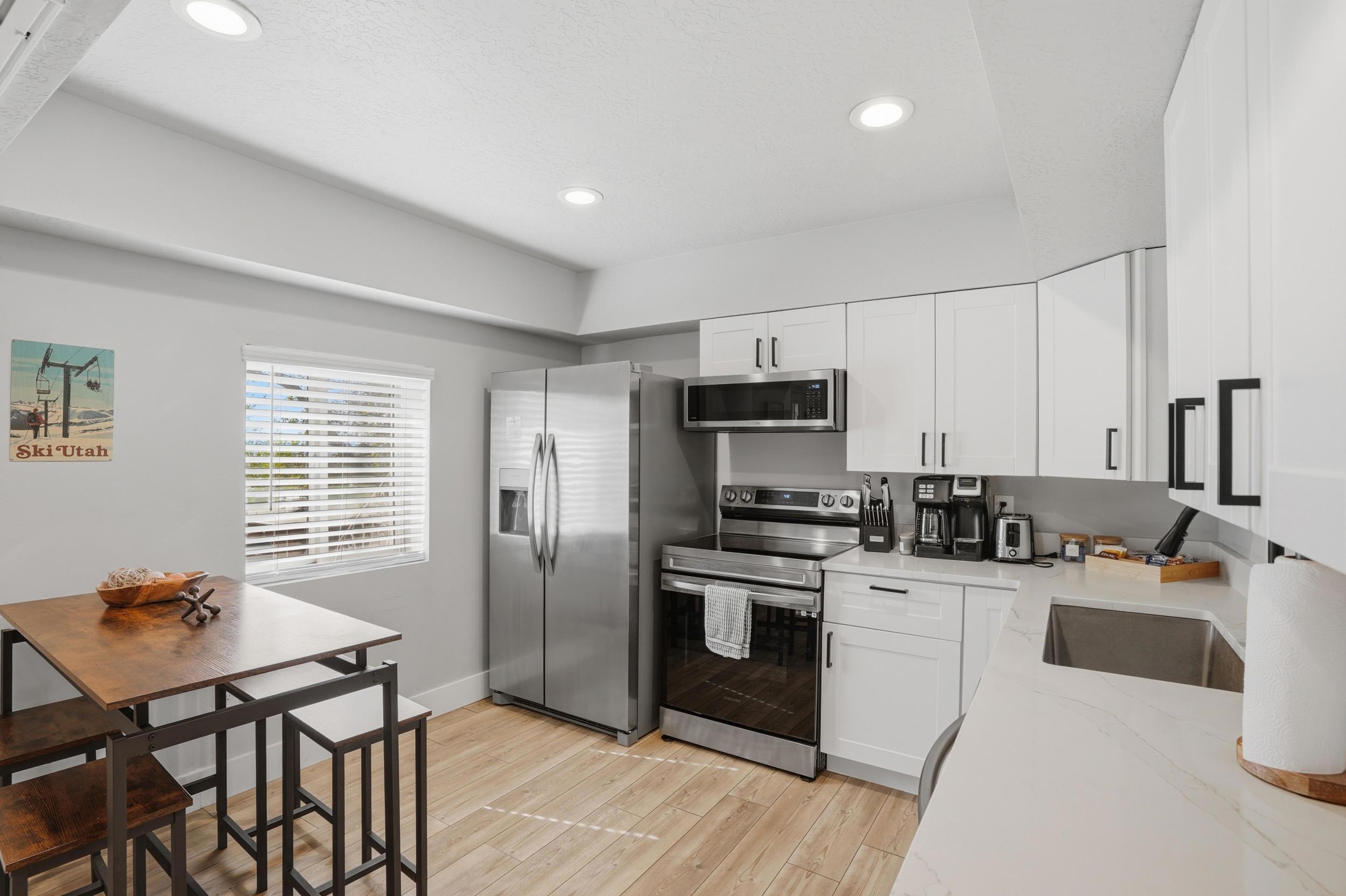Furnished Unit #44 faces West. Kitchen with stainless steel appliances, white cabinets, light wood-style flooring, light stone countertops, and recessed lighting