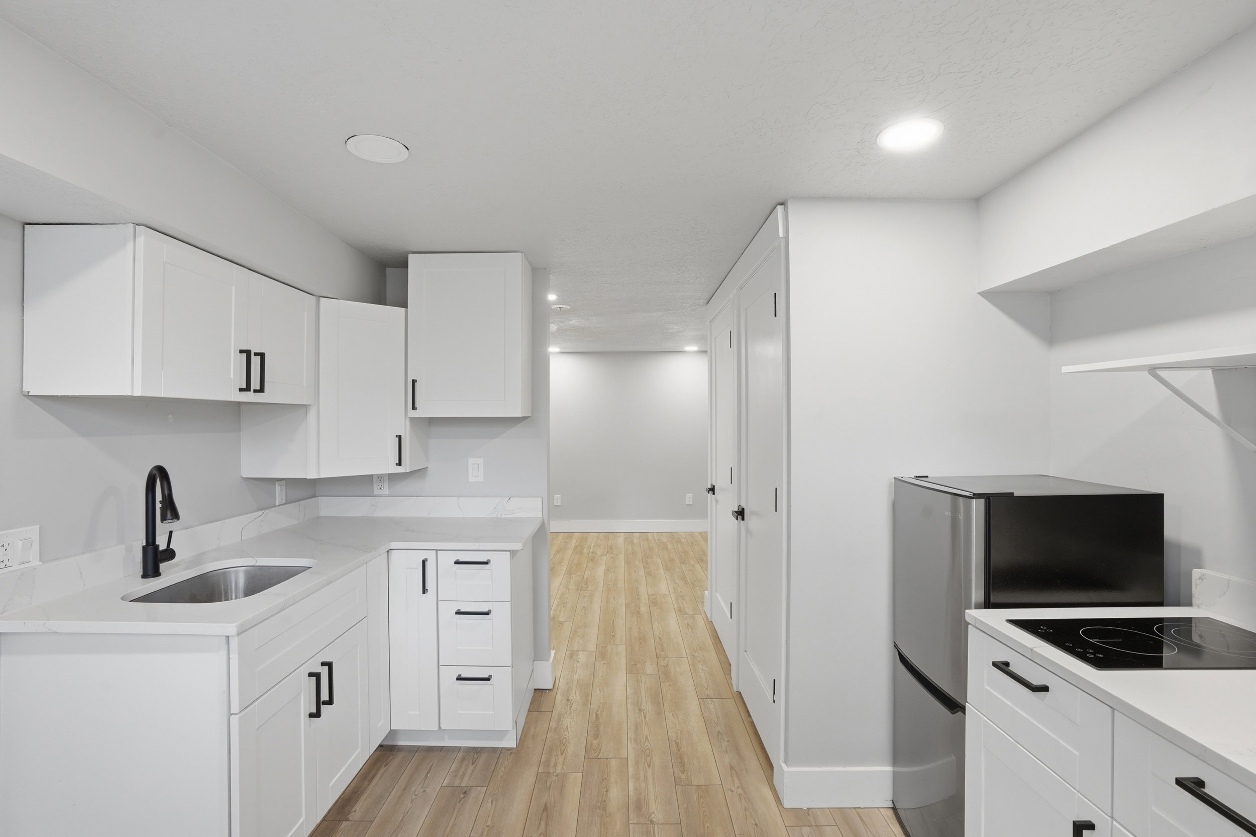 Unit #40 studio apartment with separate entrance.Kitchen featuring white cabinetry, light wood-style floors, recessed lighting, and black electric cooktop